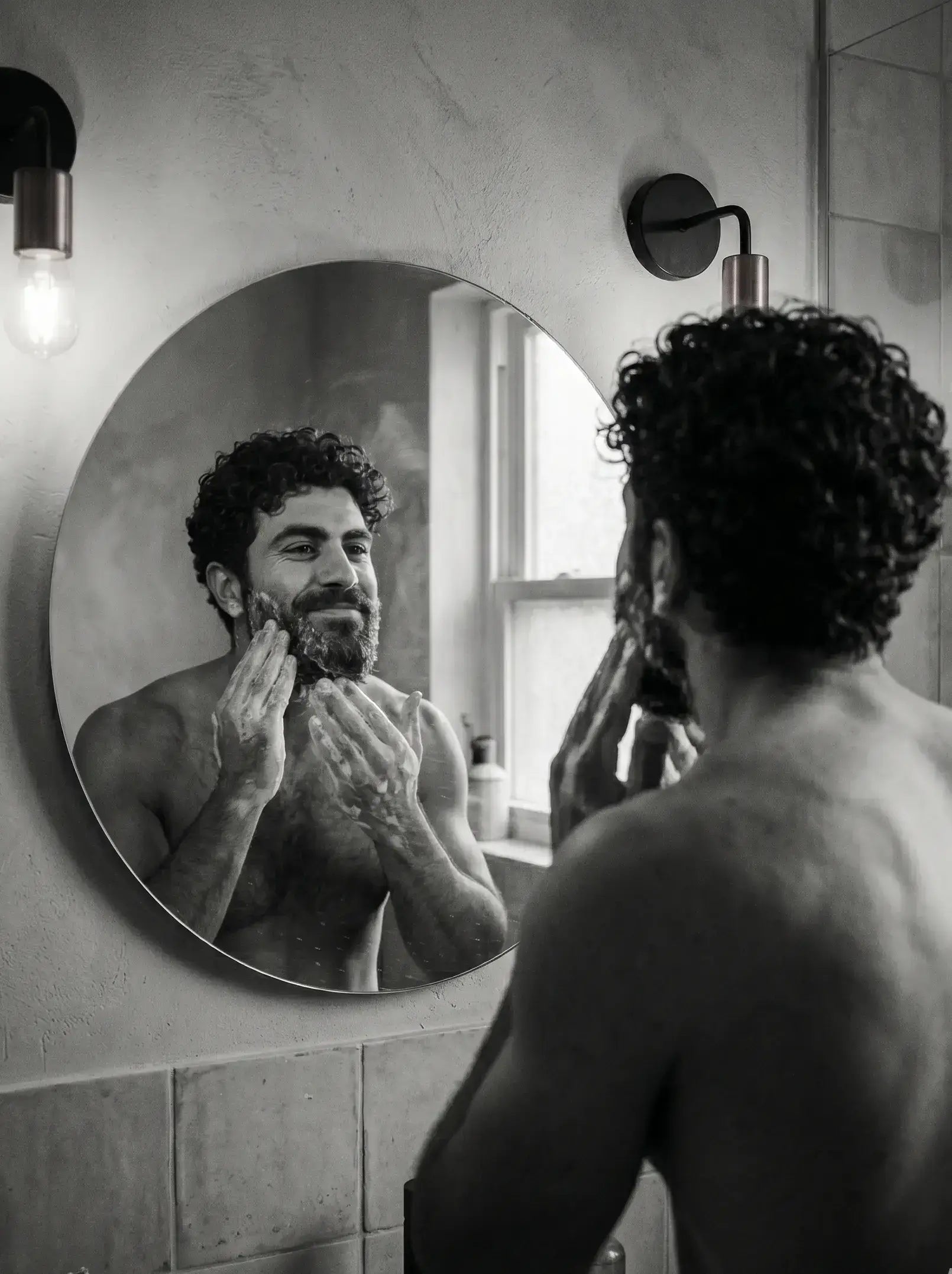 Man grooming himself in front of a mirror in a bathroom.